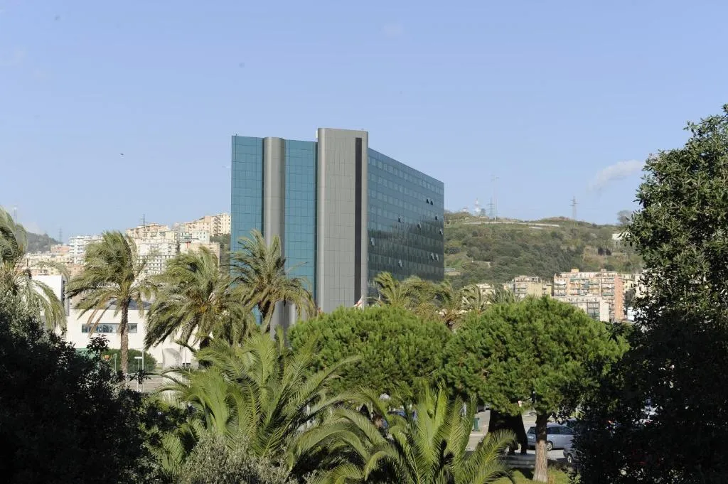 Veduta esterna dell'hotel a torre con facciata in vetro circondato da palme e vegetazione