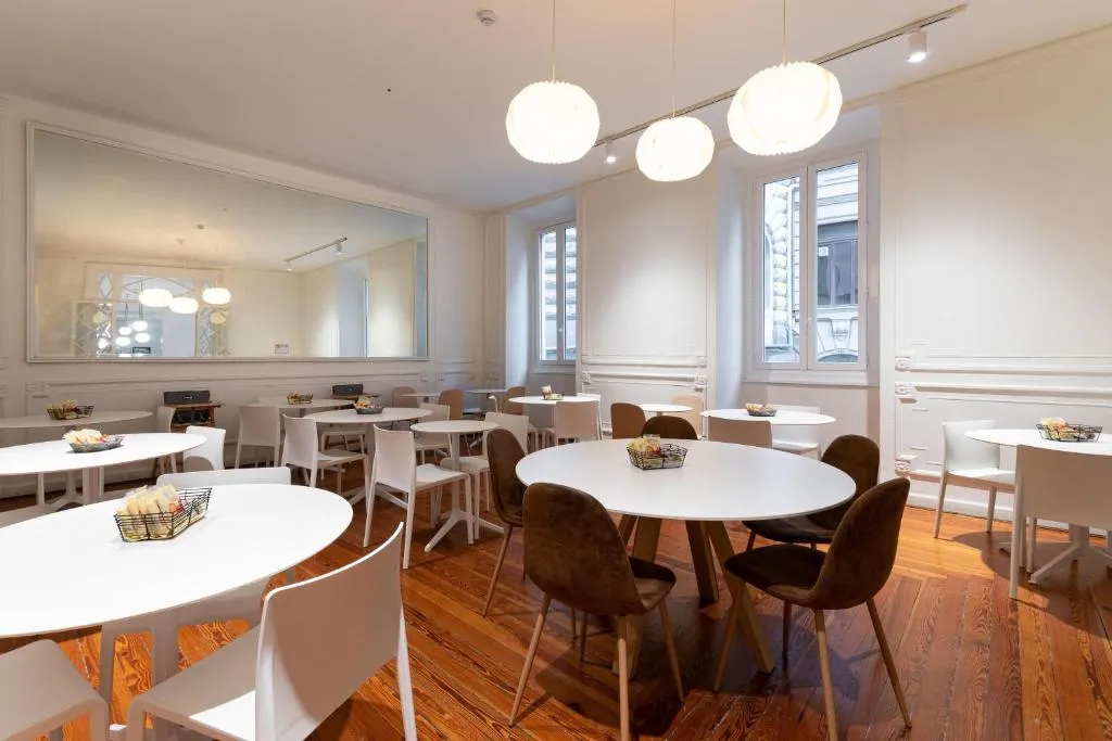 Sala colazione luminosa con tavoli rotondi bianchi e lampade a sospensione