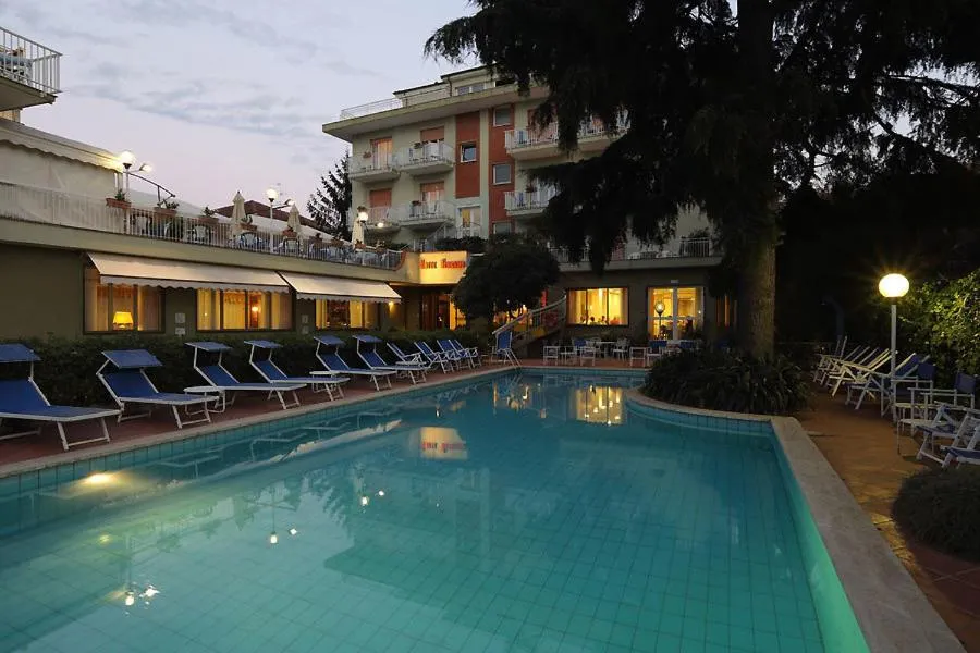 Piscina dell'hotel al tramonto con lettini e edificio illuminato sullo sfondo