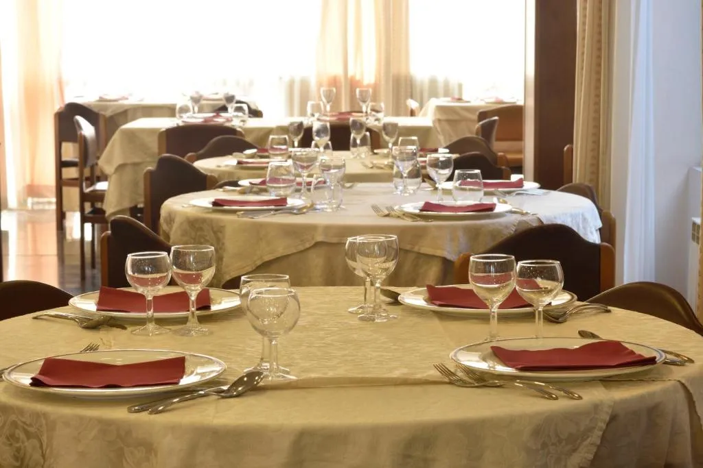 Sala ristorante con tavoli rotondi apparecchiati con tovaglioli rossi e bicchieri