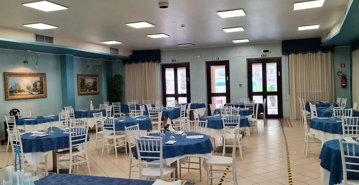 Sala ristorante con tavoli tondi apparecchiati con tovaglie blu e sedie bianche