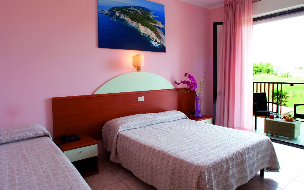 Camera tripla in tonalità rosa con letti, quadro marino e balcone