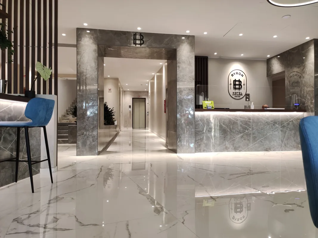 Hall dell'hotel con reception in marmo, pavimento lucido e sgabelli blu