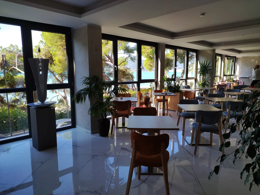 Sala ristorante con tavoli, sedie colorate, grandi vetrate e vista sulla vegetazione e sul mare