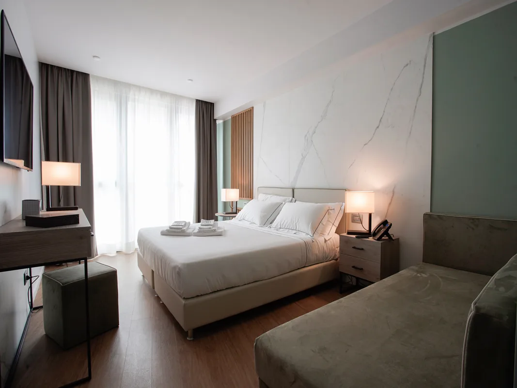 Elegante camera con parete in marmo, letto matrimoniale, lampade e divanetto