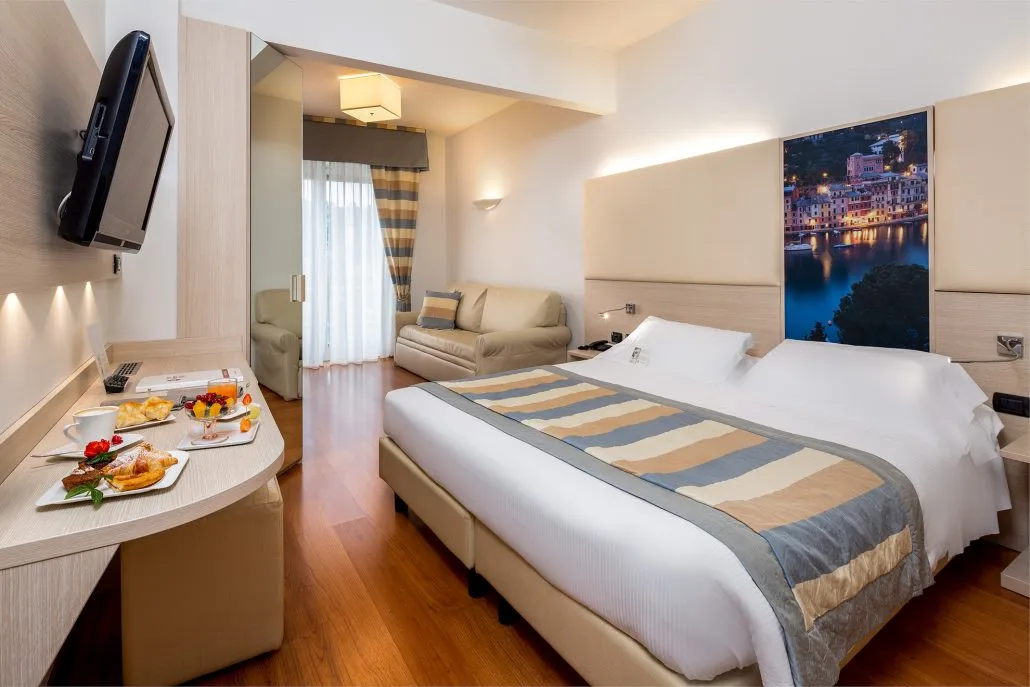 Camera matrimoniale con divano, TV e testiera decorata con immagine di Portofino