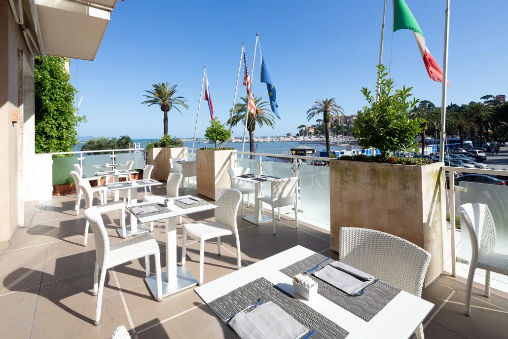 Terrazza ristorante con tavoli bianchi, vista sul porto e bandiere internazionali
