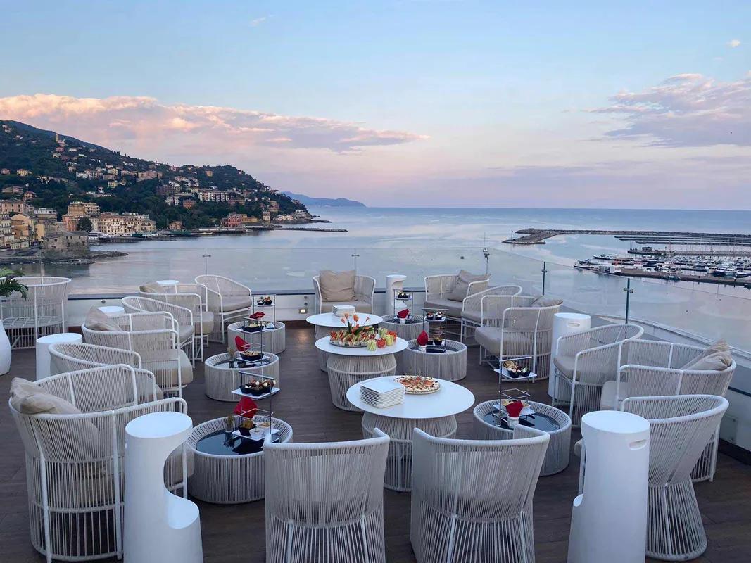 Terrazza panoramica con poltrone bianche e aperitivo al tramonto sulla baia
