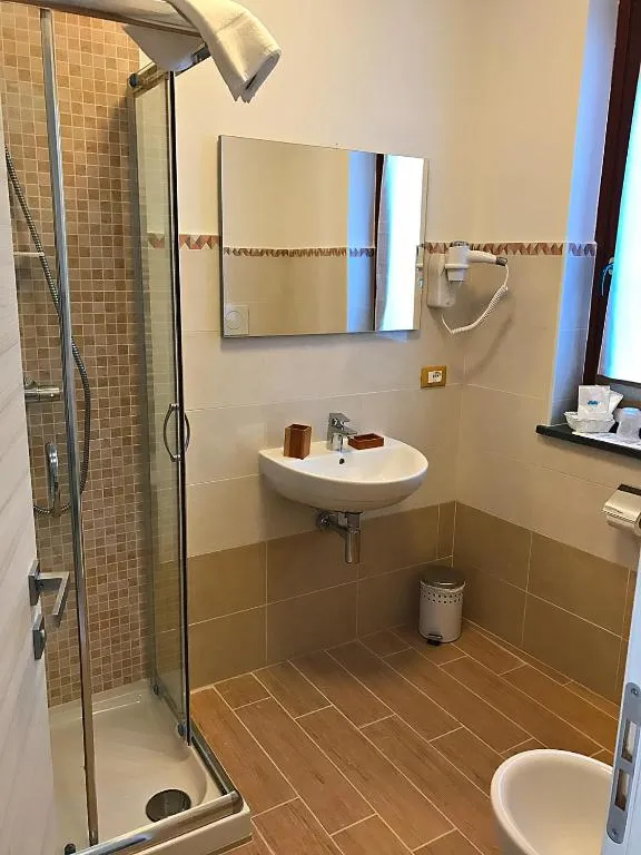 Bagno con doccia in vetro, lavabo e pavimento effetto legno
