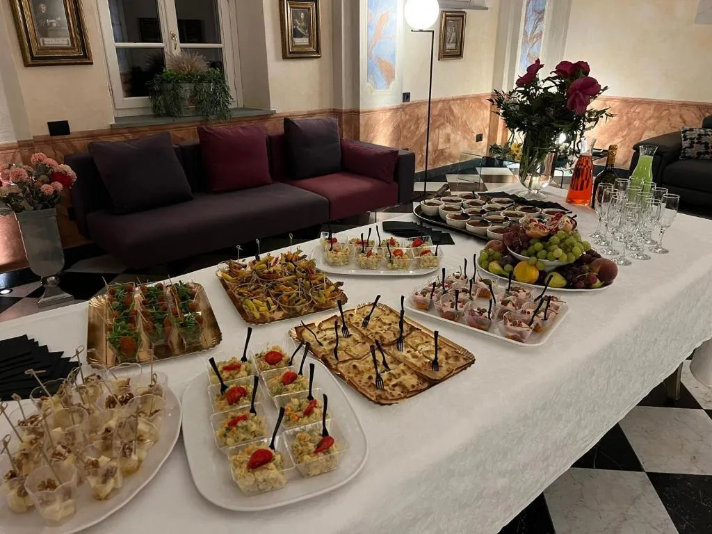 Buffet di finger food e dolci allestito su tavolo bianco in una sala elegante con affreschi