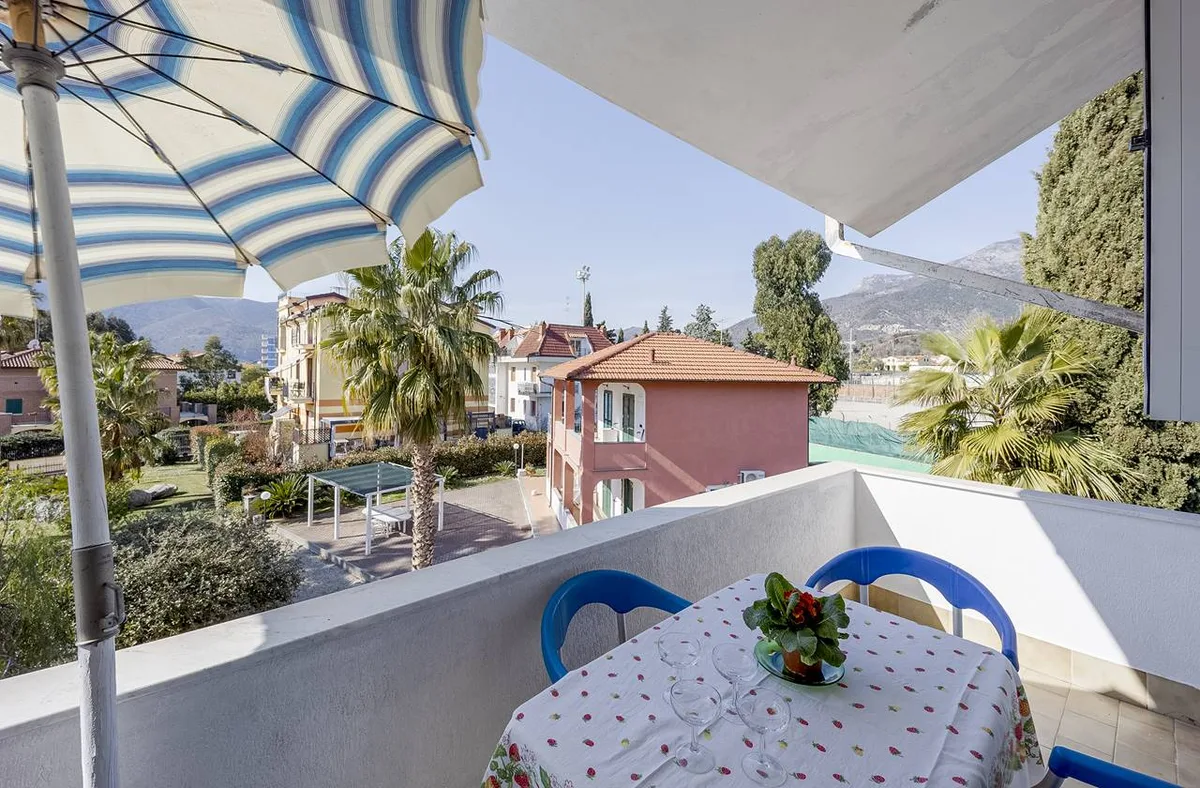 Balcone con ombrellone a righe, tavolo apparecchiato e vista su palme e montagne