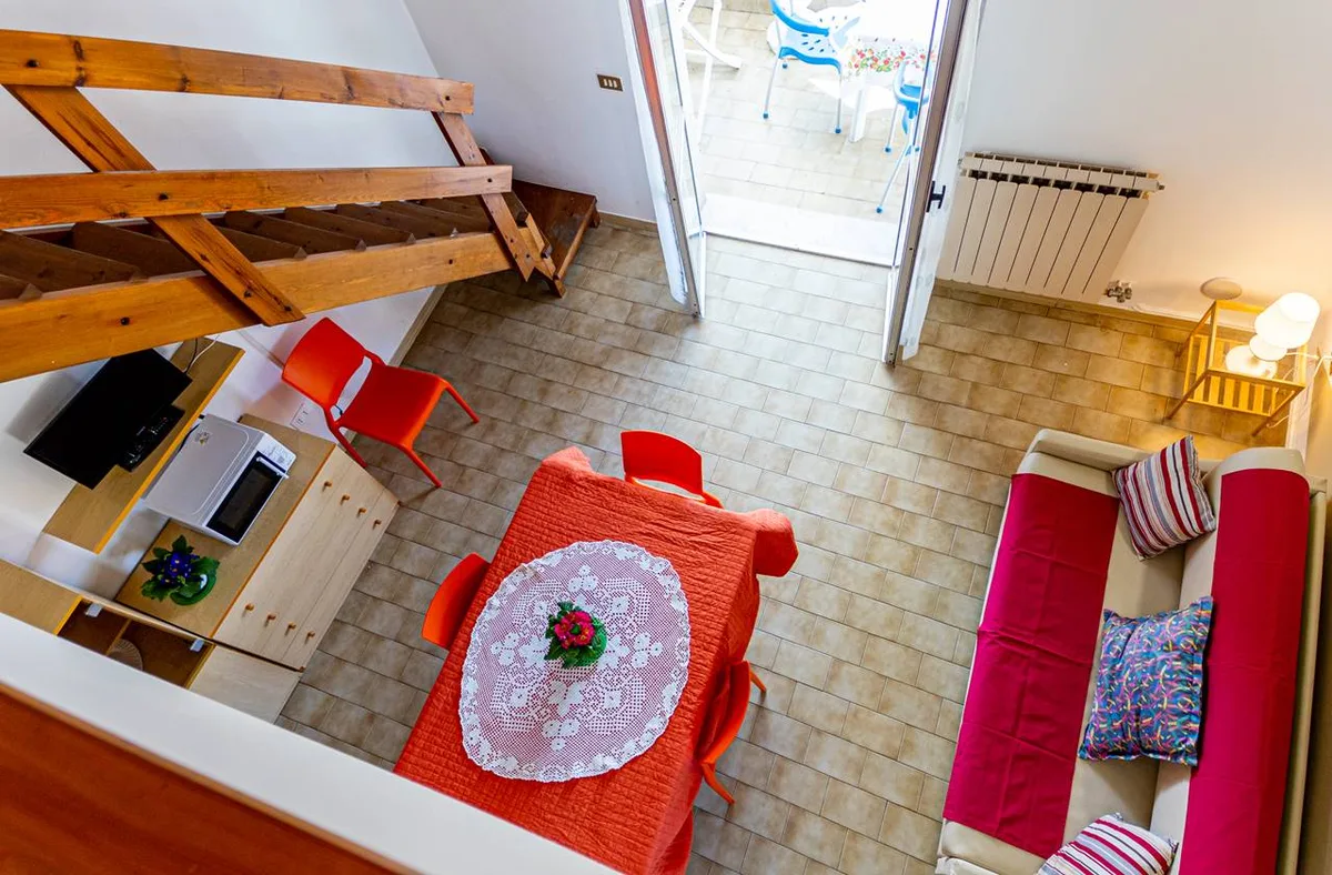 Vista dall'alto di appartamento su due livelli con scala in legno, tavolo e divano