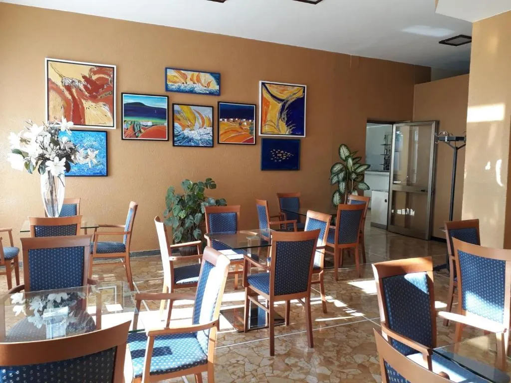 Sala soggiorno con tavoli in vetro, sedie blu e parete decorata con dipinti marini colorati
