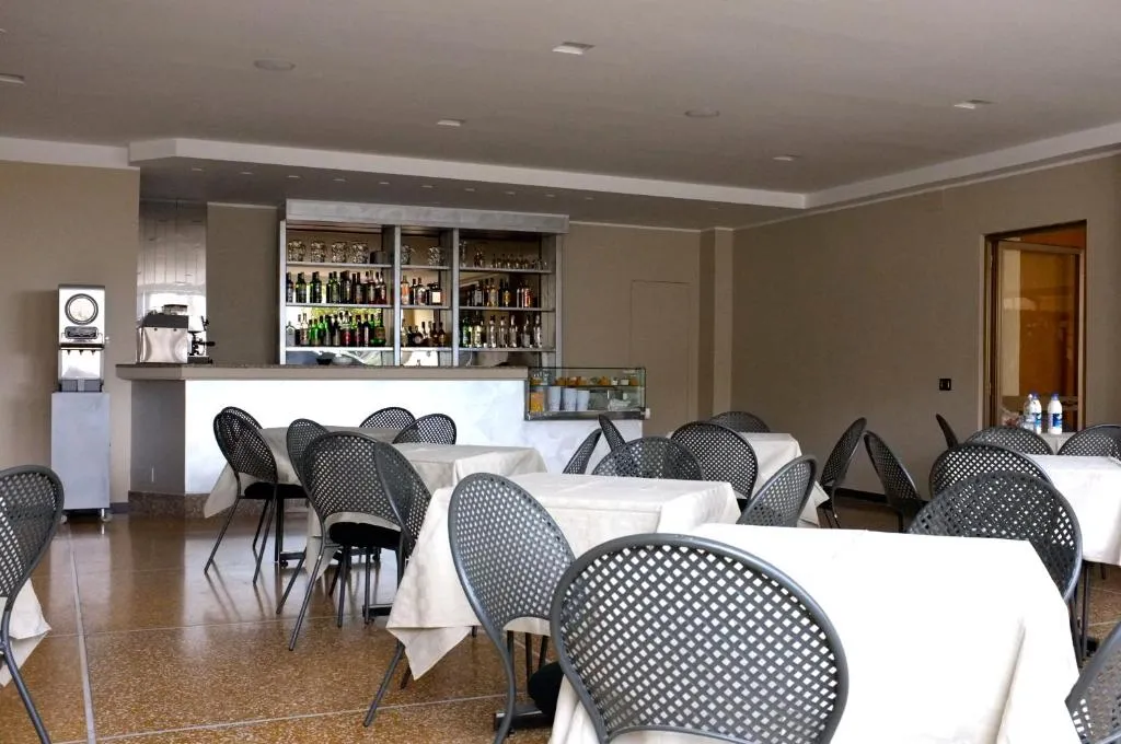 Sala bar con tavoli apparecchiati, sedie scure e bancone con bottiglie alle spalle