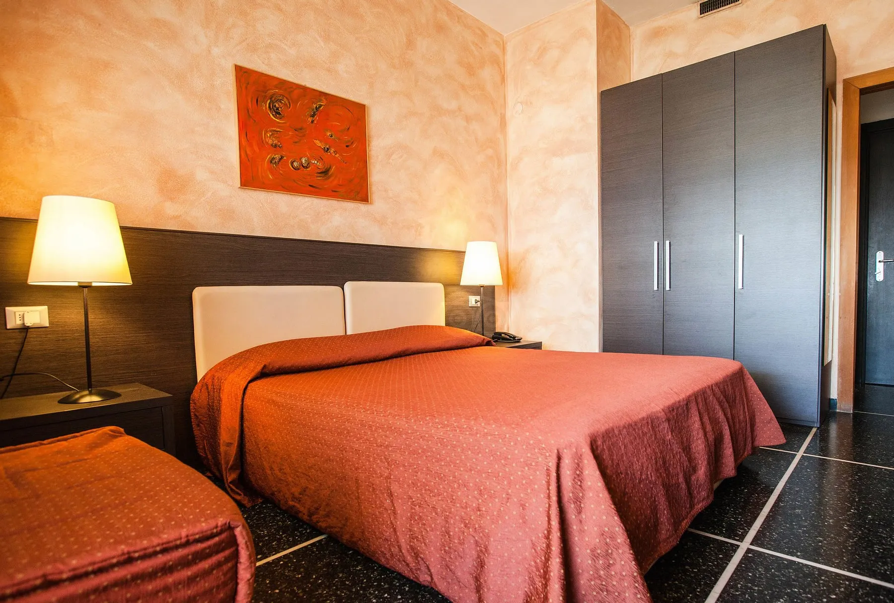 Camera con letto matrimoniale, copriletto rosso, armadio scuro e lampade da comodino