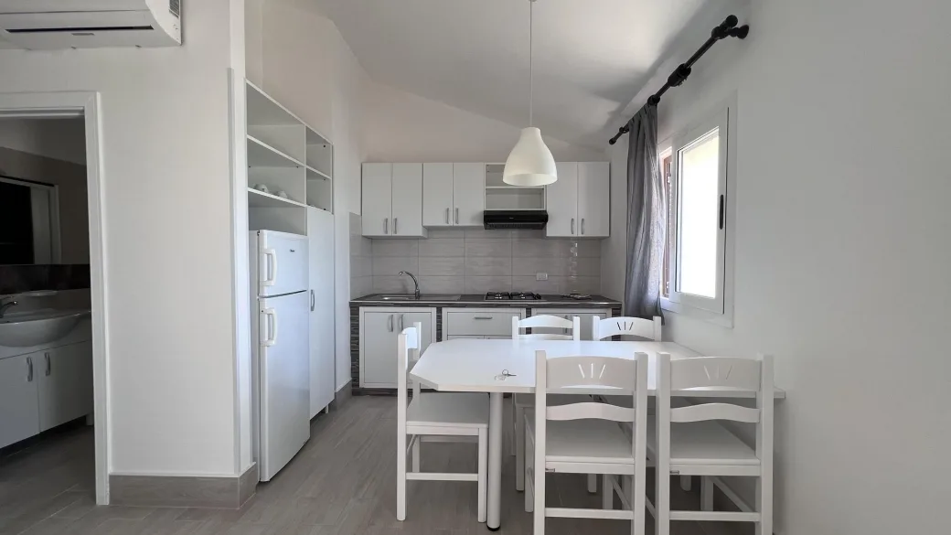Cucina moderna bianca con tavolo da pranzo, sedie, frigorifero e aria condizionata
