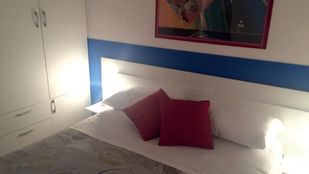 Dettaglio di camera da letto con cuscini rossi, armadio bianco e quadro alla parete