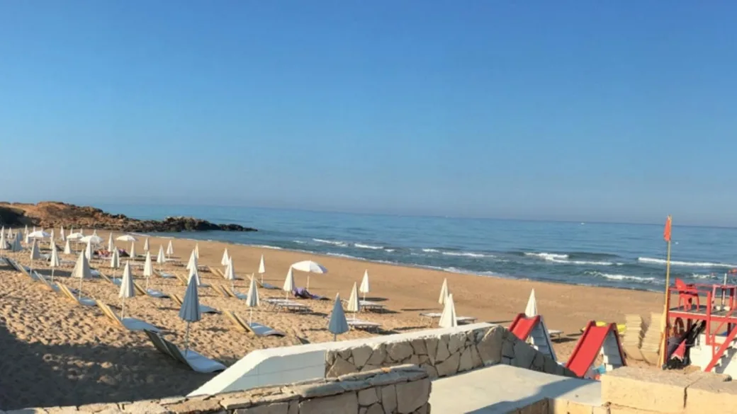 Spiaggia sabbiosa attrezzata con lettini e ombrelloni chiusi affacciata sul mare calmo