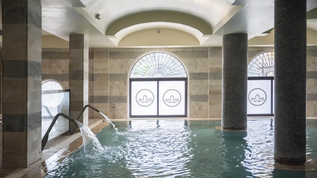 Piscina interna con getto d'acqua, colonne in marmo e vetrate decorate