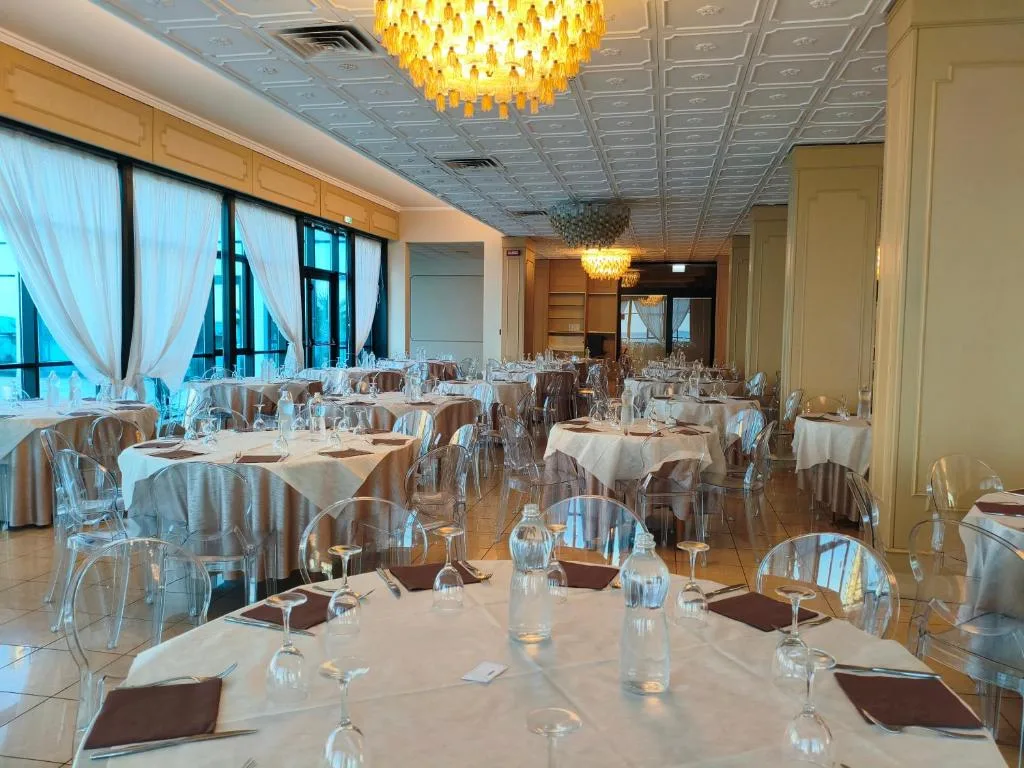 Sala ristorante con tavoli apparecchiati, sedie trasparenti e lampadari dorati