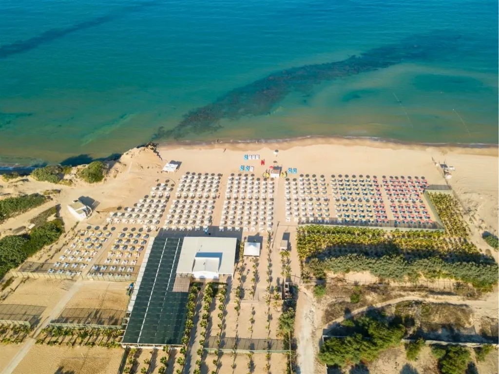 Vista dall'alto della spiaggia sabbiosa con ombrelloni ordinati e acqua turchese