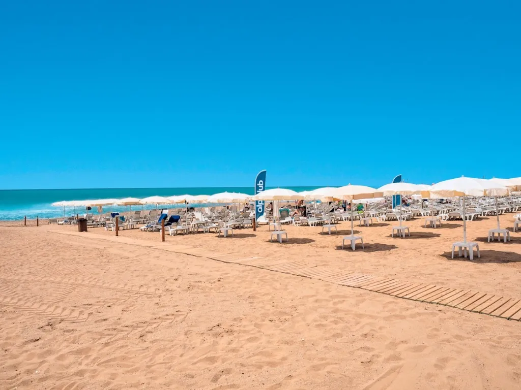 Spiaggia con ombrelloni bianchi, lettini e mare cristallino sotto cielo azzurro