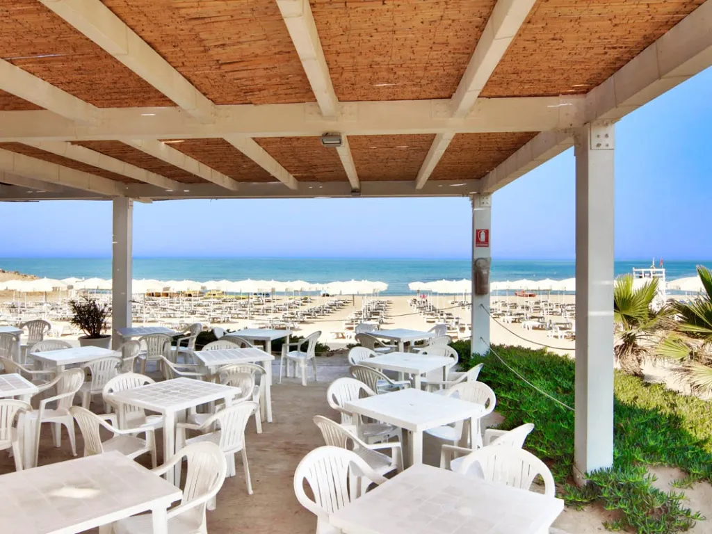Terrazza coperta sulla spiaggia con tavoli e sedie bianche e vista mare