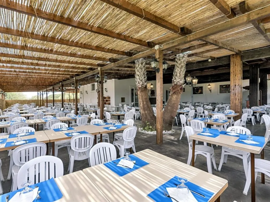 Ristorante all'aperto con pergolato in canne, tavoli con tovagliette blu e palme