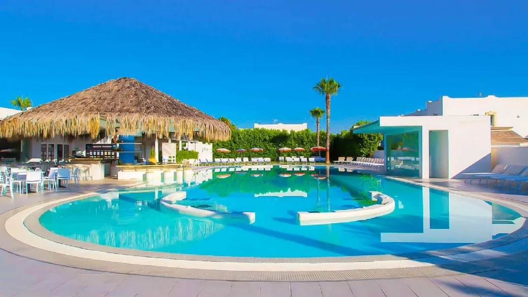 Piscina con bar in paglia, palme e zona ristoro con tavoli bianchi