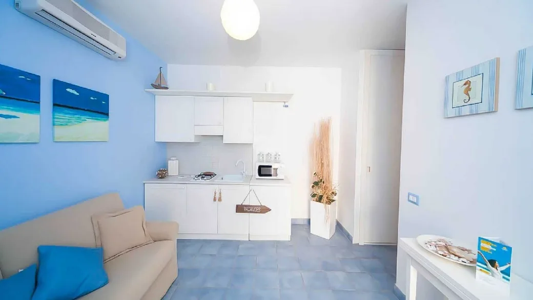 Angolo cucina e soggiorno con divano beige, cucinino bianco e dettagli in stile marino