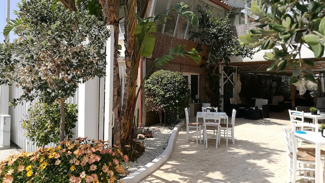 Area lounge esterna con tavoli bianchi e divani tra il verde