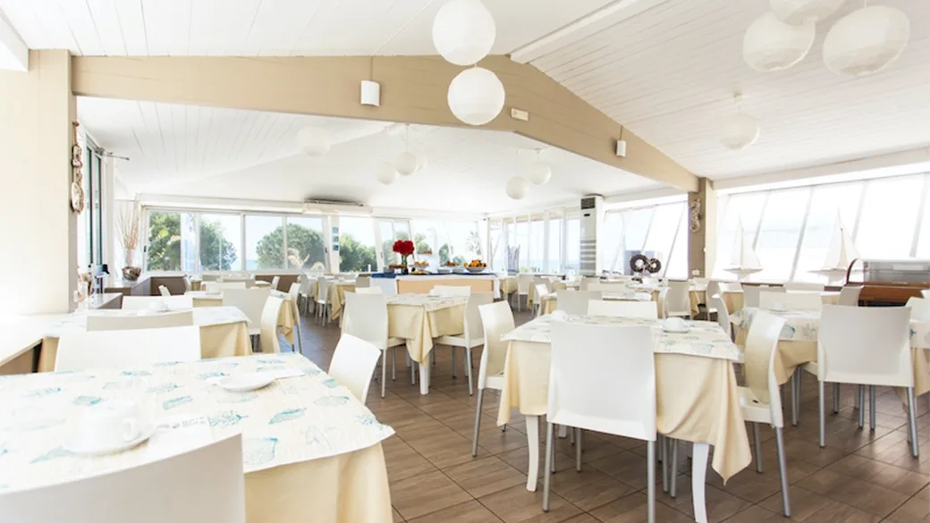 Sala ristorante luminosa con tavoli bianchi e ampie vetrate