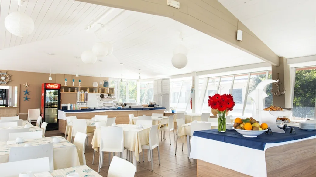Sala colazione con buffet, tavoli bianchi e decorazioni floreali