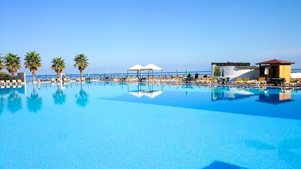 Grande piscina con lettini, palme e vista sul mare