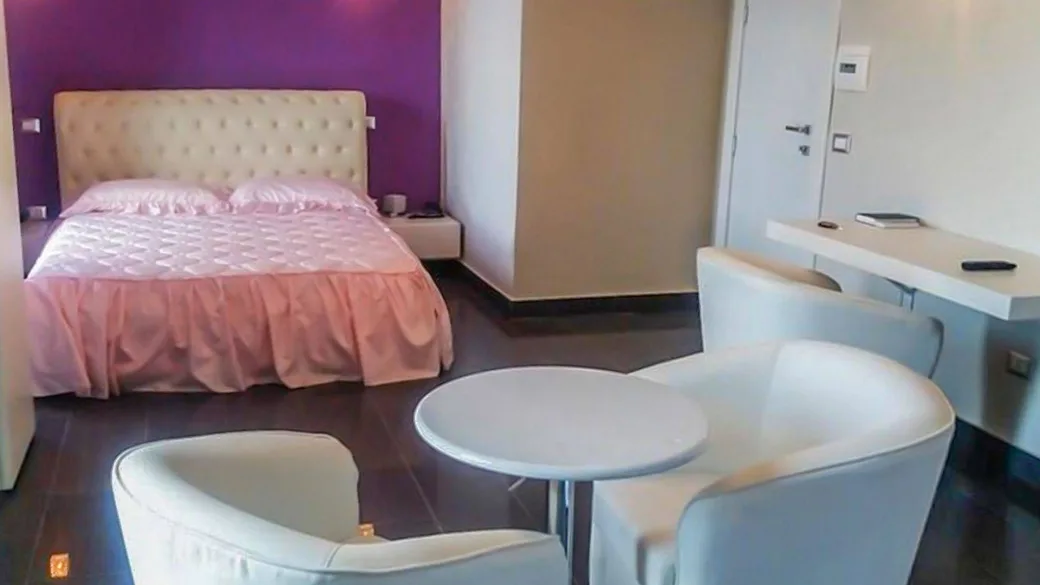 Camera con letto matrimoniale, parete viola, tavolino e poltrone bianche