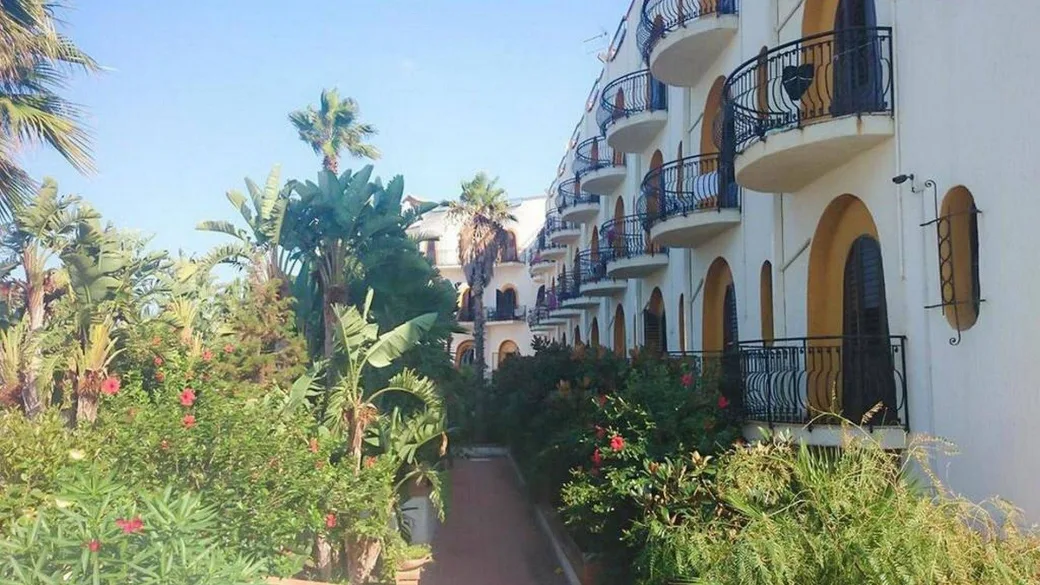 Facciata dell'hotel con balconi tra giardino tropicale e palme