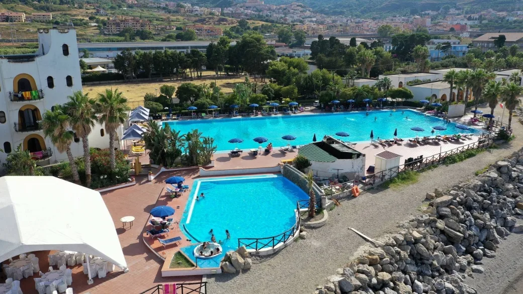 Veduta aerea di due piscine con ombrelloni e lettini vicino alla spiaggia