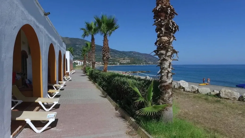 Vialetto lungomare con lettini, archi e palme accanto alla spiaggia