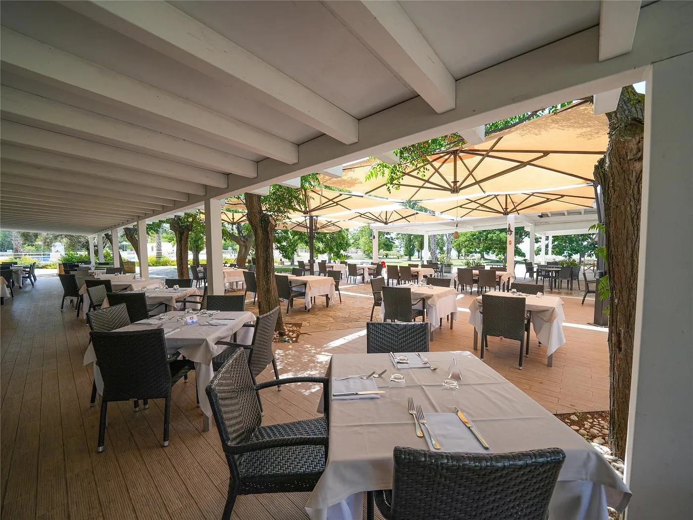 Terrazza ristorante coperta con tavoli e ombrelloni nel verde