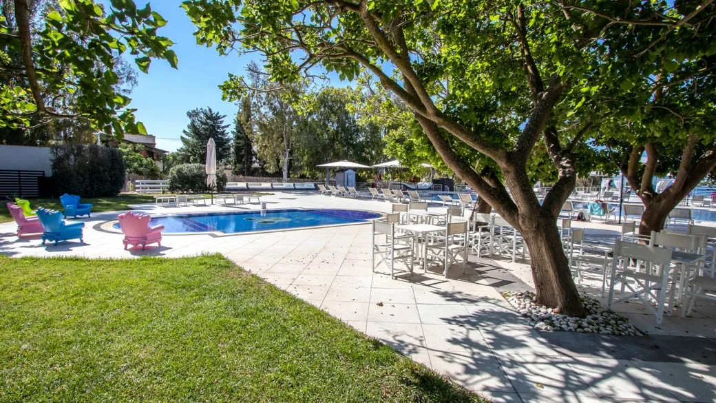 Piscina con poltrone colorate e tavoli all'ombra degli alberi