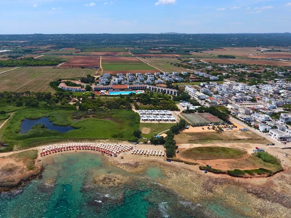 Vista aerea del resort sulla costa con piscina, edifici bianchi e spiaggia con ombrelloni