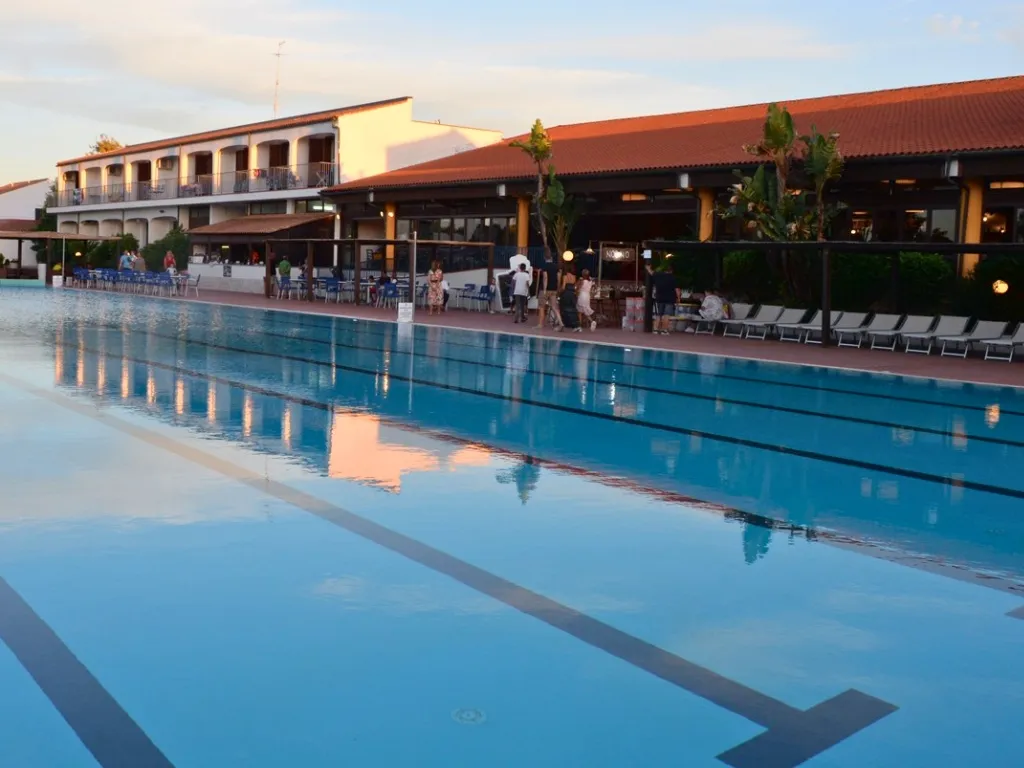 Piscina al tramonto con edifici del resort e ospiti a bordo vasca