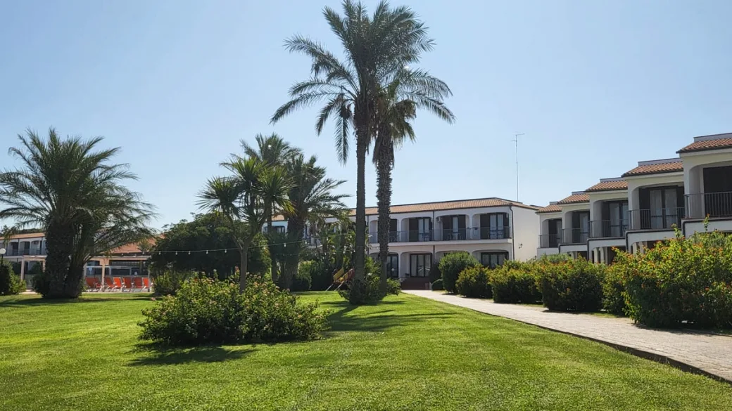 Vialetto del resort tra prato verde, palme e edifici bianchi a due piani