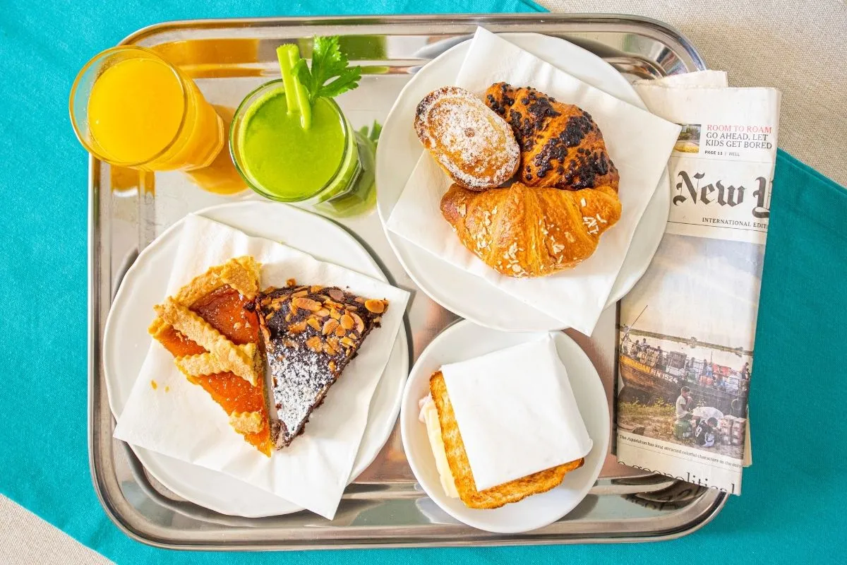Vassoio con colazione dolce, cornetti, succhi e giornale