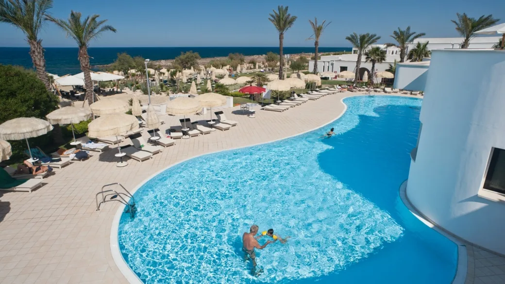Piscina curva del resort con lettini, ombrelloni in paglia e vista sul mare