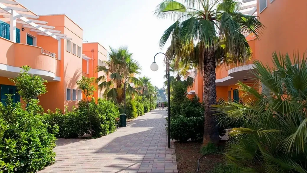 Viale alberato con palme tra le palazzine arancioni del resort
