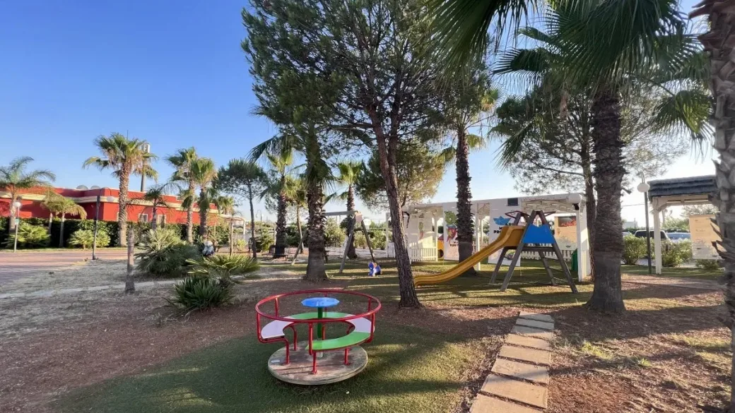 Area giochi per bambini con scivolo e giostrina tra le palme