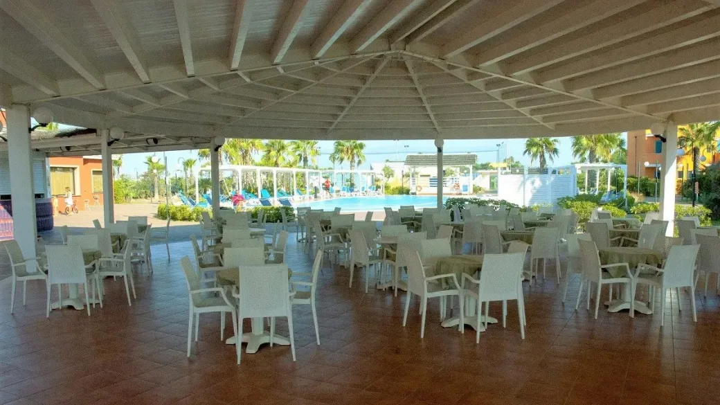 Area bar coperta con tavoli e sedie bianche vista piscina