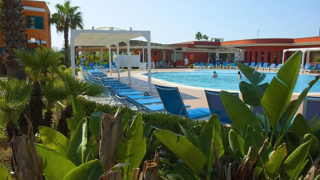 Piscina con lettini blu vista dal giardino tropicale