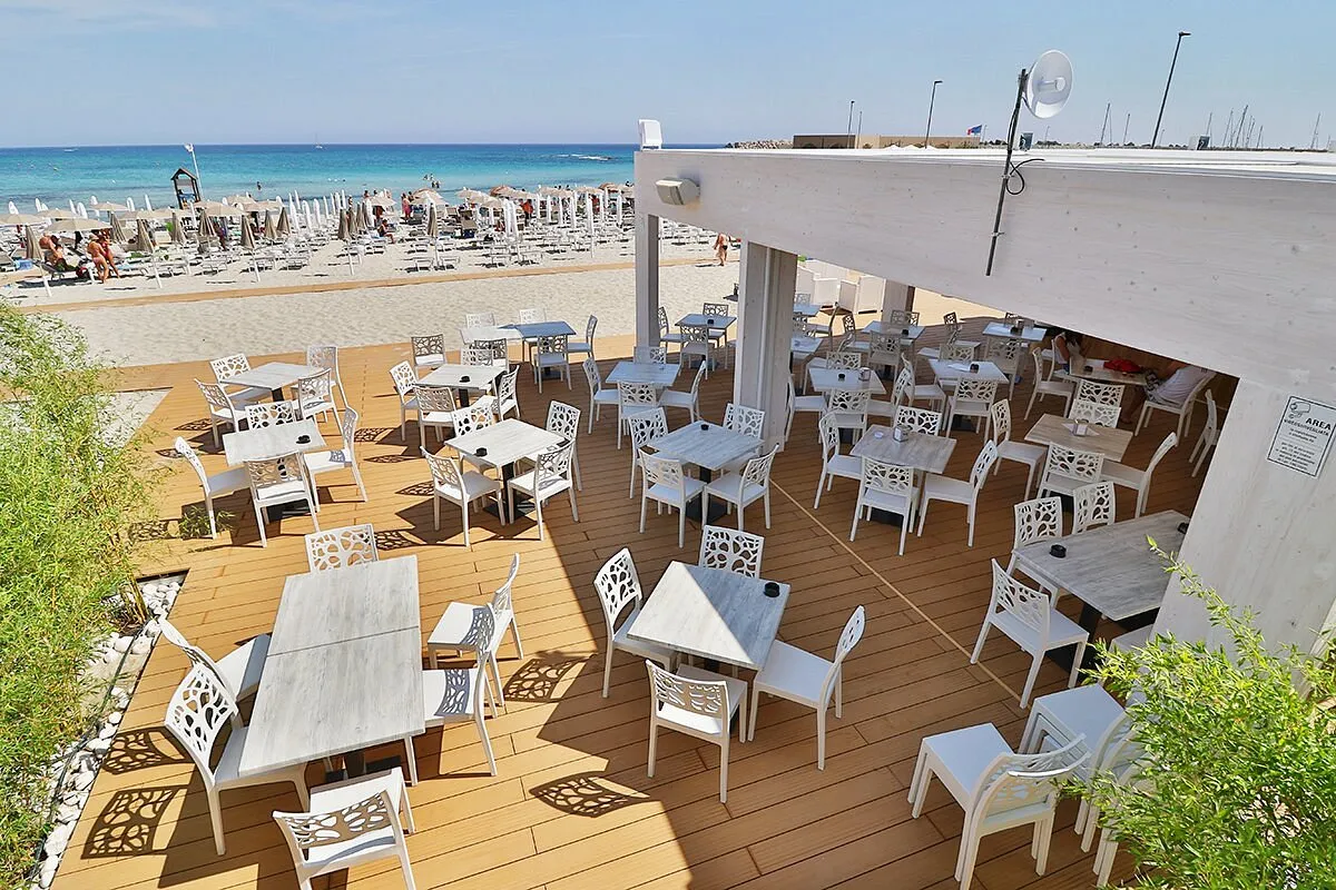 Terrazza ristorante sul mare con tavoli e sedie bianche affacciati sulla spiaggia